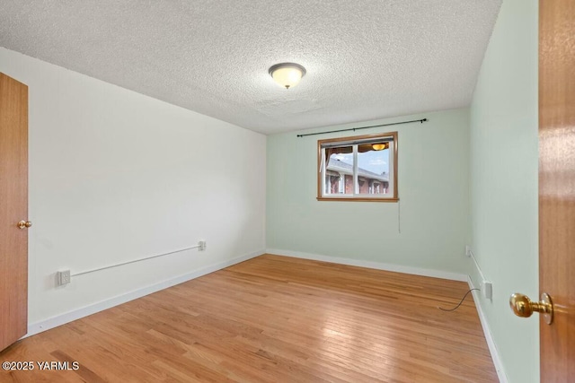 spare room featuring baseboards, a textured ceiling, and light wood finished floors