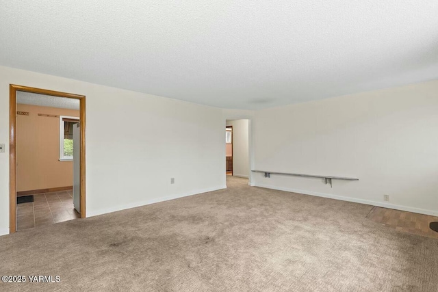 empty room featuring light carpet, a textured ceiling, and baseboards