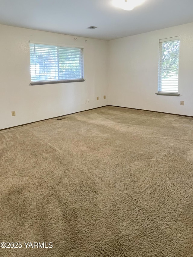 carpeted empty room featuring baseboards, visible vents, and plenty of natural light