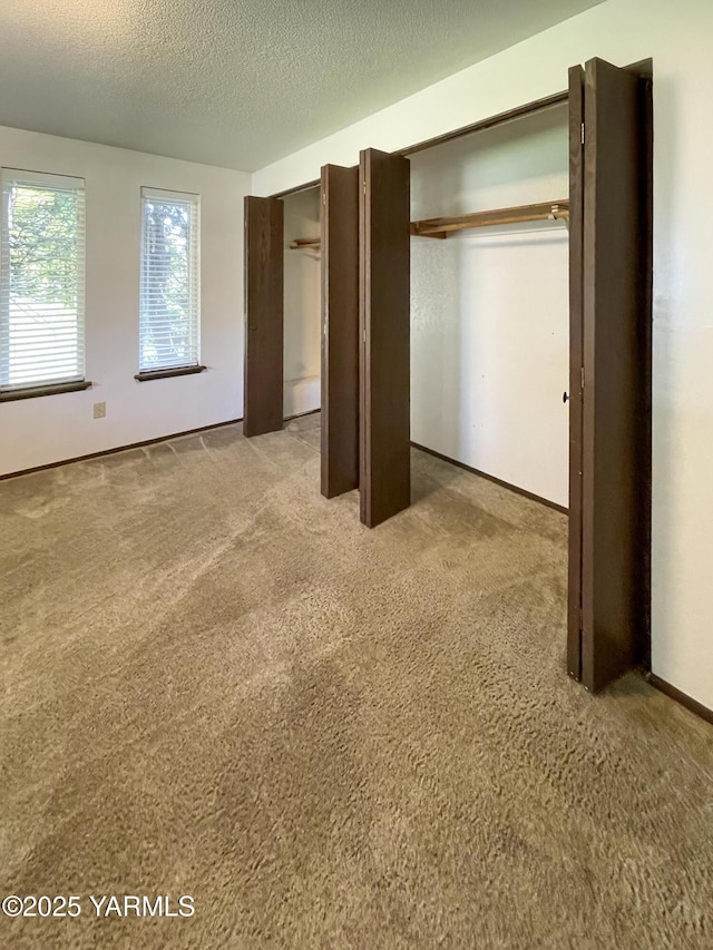 unfurnished bedroom featuring a textured ceiling, multiple closets, baseboards, and carpet