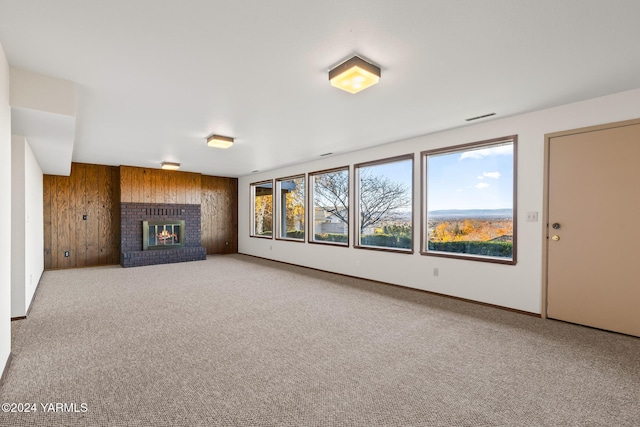 unfurnished living room featuring carpet floors, a fireplace, visible vents, wooden walls, and baseboards