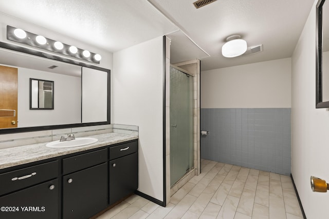 full bath featuring a textured ceiling, vanity, visible vents, tile walls, and a shower stall