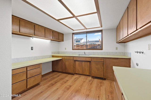 kitchen featuring a sink, light wood-style floors, light countertops, built in study area, and brown cabinets