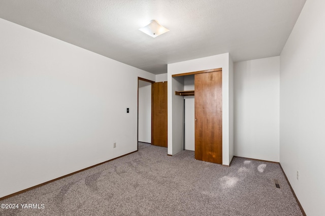 unfurnished bedroom featuring a textured ceiling, visible vents, a closet, and light colored carpet