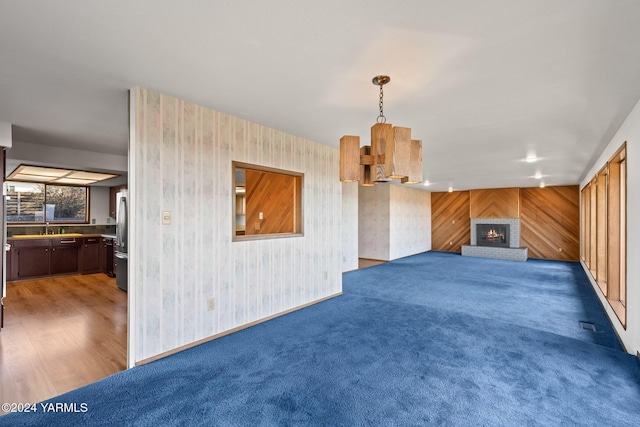 unfurnished living room featuring baseboards, dark colored carpet, a brick fireplace, and wallpapered walls