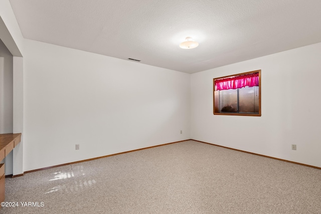 carpeted empty room featuring visible vents, a textured ceiling, and baseboards