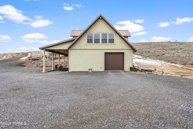 view of property exterior with gravel driveway, stucco siding, a standing seam roof, metal roof, and a garage