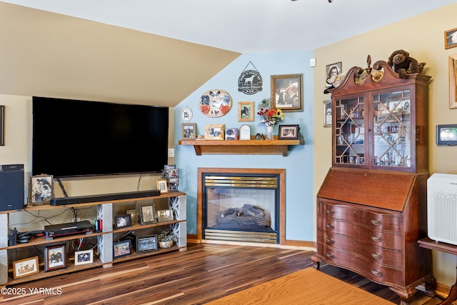 living room with lofted ceiling, wood finished floors, a glass covered fireplace, and baseboards