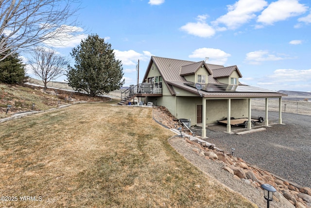 view of home's exterior with metal roof, stairs, a lawn, a wooden deck, and stucco siding