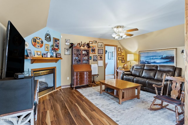 living area featuring a ceiling fan, lofted ceiling, a glass covered fireplace, and wood finished floors