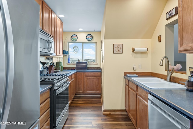 kitchen featuring brown cabinetry, dark countertops, appliances with stainless steel finishes, dark wood-type flooring, and a sink