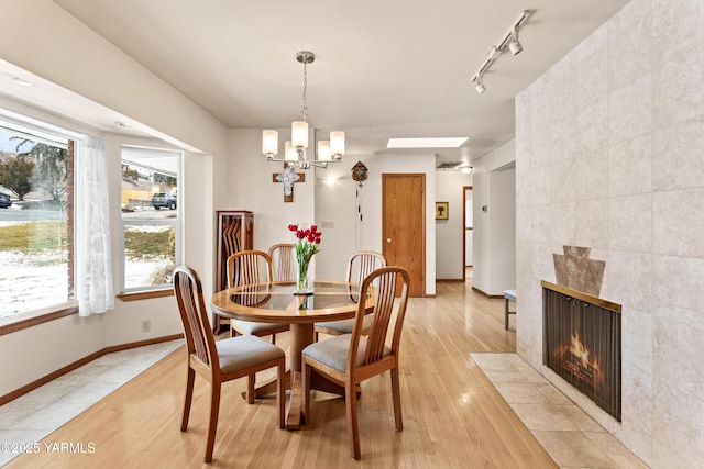 dining area featuring a skylight, a fireplace, rail lighting, light wood-style floors, and baseboards