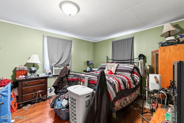 bedroom featuring a textured wall, ornamental molding, a textured ceiling, wood finished floors, and cooling unit