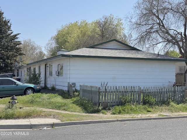 view of side of home featuring cooling unit, a shingled roof, and fence