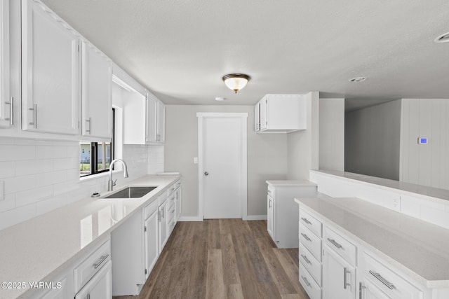 kitchen featuring dark wood-style floors, a textured ceiling, a sink, white cabinetry, and decorative backsplash