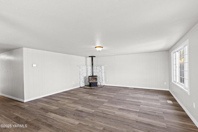 unfurnished living room featuring baseboards, wood finished floors, and a wood stove