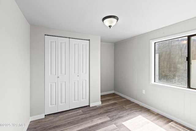 unfurnished bedroom featuring a closet, wood finished floors, visible vents, and baseboards