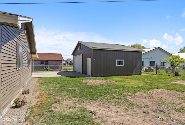 view of yard featuring concrete driveway, fence, an outbuilding, and a detached garage
