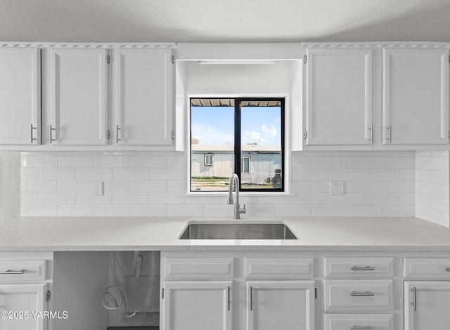 kitchen featuring decorative backsplash, white cabinetry, a sink, and light countertops
