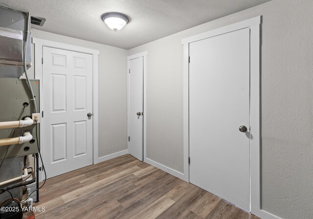 interior space with heating unit, wood finished floors, a textured ceiling, baseboards, and visible vents