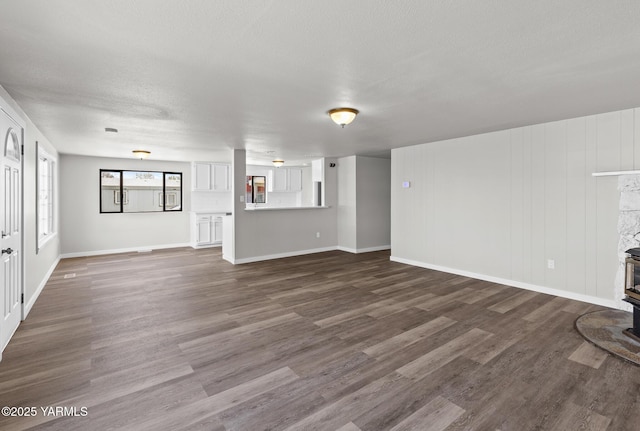 unfurnished living room featuring baseboards, a wood stove, and dark wood-style floors