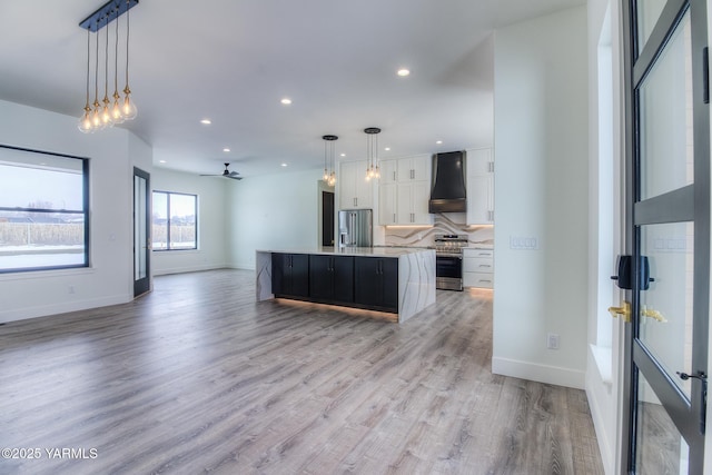 kitchen featuring decorative light fixtures, a spacious island, open floor plan, white cabinetry, and wall chimney exhaust hood