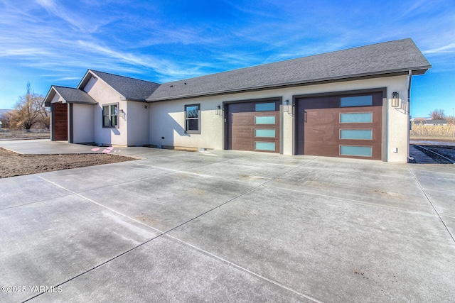 view of front of house featuring a garage, concrete driveway, roof with shingles, and stucco siding