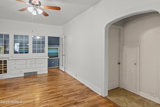 spare room featuring ceiling fan, arched walkways, light wood finished floors, baseboards, and visible vents