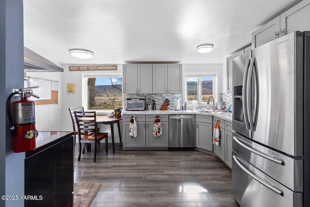 kitchen with decorative backsplash, gray cabinets, appliances with stainless steel finishes, plenty of natural light, and dark wood-style flooring