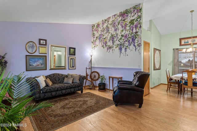 living area with baseboards, high vaulted ceiling, light wood-style flooring, and an inviting chandelier