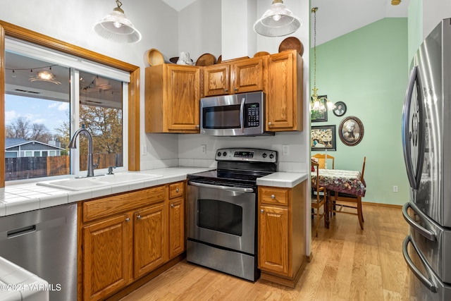 kitchen featuring tile countertops, brown cabinets, hanging light fixtures, stainless steel appliances, and a sink