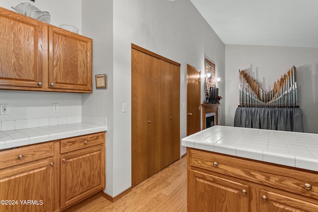 kitchen with tile countertops, light wood-type flooring, a fireplace, and brown cabinets