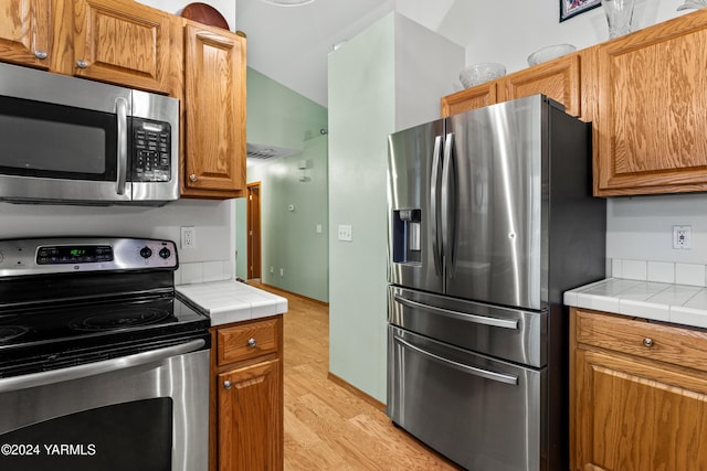 kitchen featuring stainless steel appliances, brown cabinetry, and tile countertops