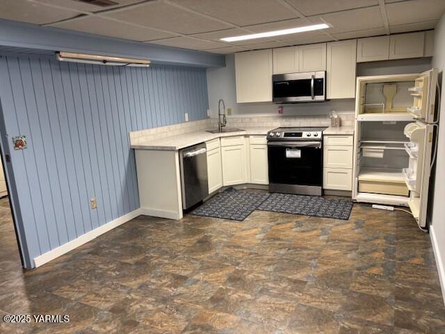 kitchen featuring appliances with stainless steel finishes, a sink, baseboards, a drop ceiling, and white cabinetry