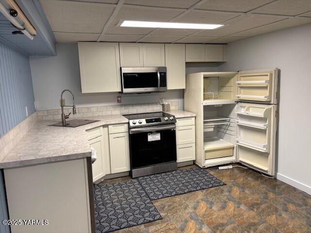 kitchen with stone finish floor, light countertops, a paneled ceiling, a sink, and stainless steel appliances