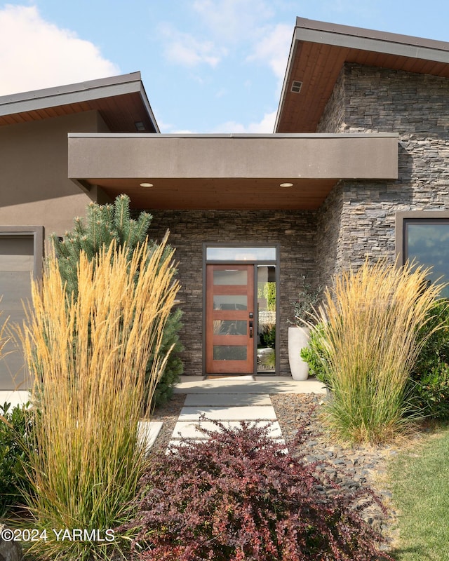 view of exterior entry featuring stone siding and stucco siding