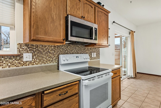 kitchen with tasteful backsplash, white range with electric stovetop, stainless steel microwave, and light countertops