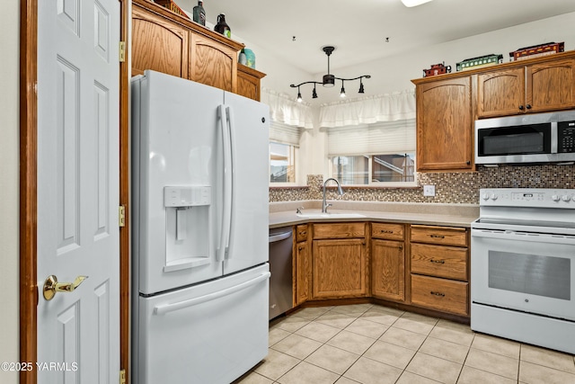 kitchen featuring stainless steel appliances, light countertops, brown cabinetry, light tile patterned flooring, and a sink