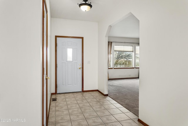 entryway featuring light carpet, light tile patterned floors, baseboards, and arched walkways