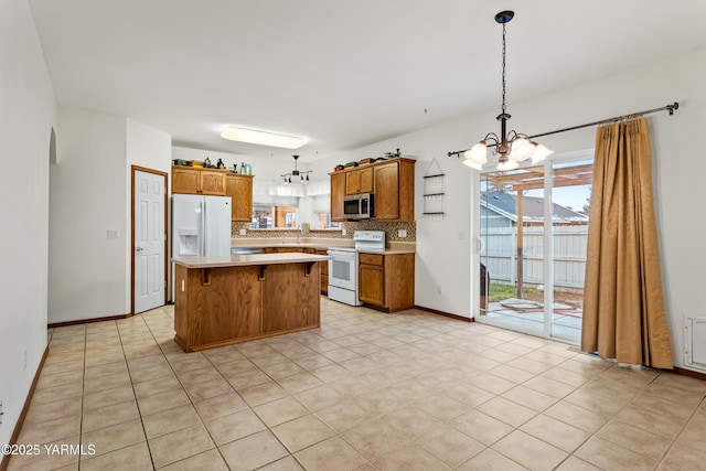 kitchen featuring a center island, pendant lighting, light countertops, brown cabinetry, and white appliances