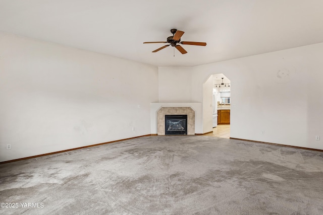 unfurnished living room featuring arched walkways, a fireplace, light colored carpet, ceiling fan, and baseboards