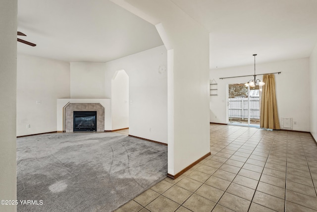 unfurnished living room with ceiling fan with notable chandelier, a tile fireplace, baseboards, and light tile patterned floors