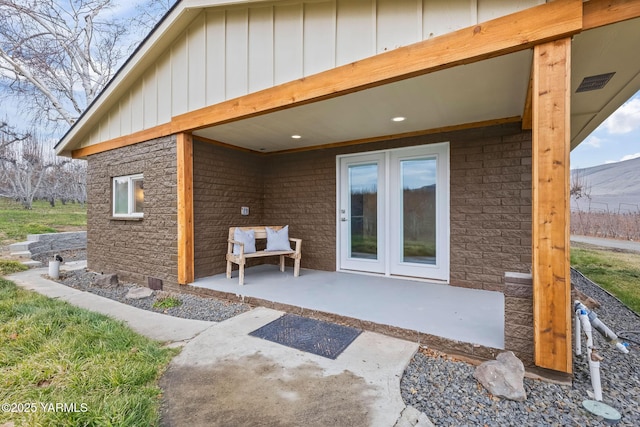 entrance to property featuring board and batten siding, stone siding, and a patio