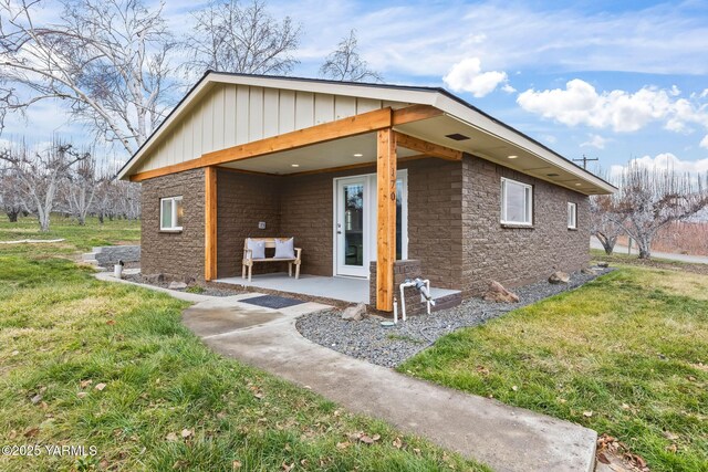 rear view of property featuring a lawn, a patio area, and board and batten siding