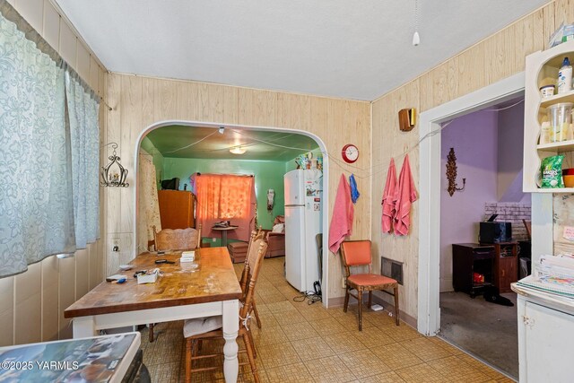 dining area with arched walkways, light floors, and wooden walls