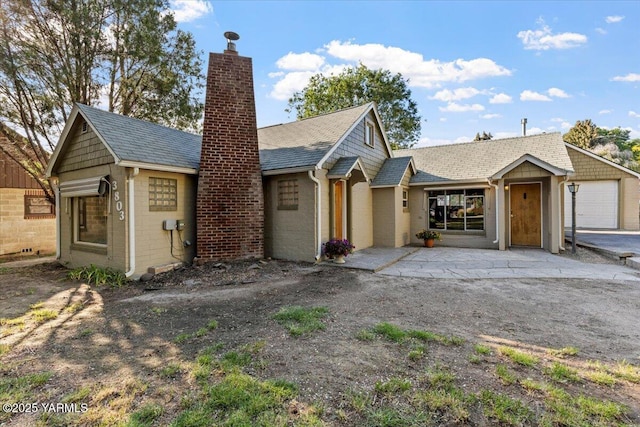 view of front facade featuring a garage, a shingled roof, and a chimney