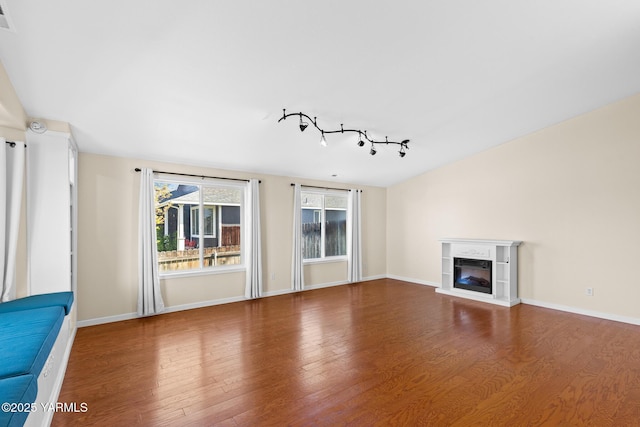 unfurnished living room with wood finished floors, a glass covered fireplace, baseboards, and track lighting