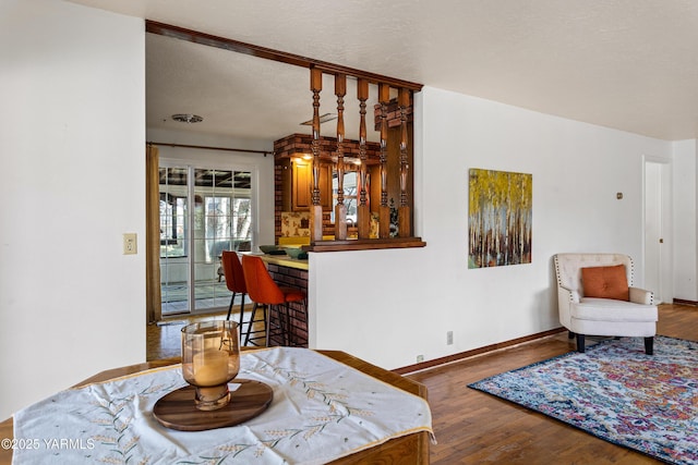 interior space with visible vents, a textured ceiling, a bar, wood finished floors, and baseboards