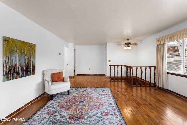 sitting room with a textured ceiling, hardwood / wood-style floors, an upstairs landing, and baseboards