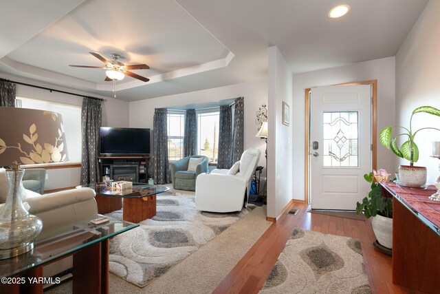 living area with light wood-type flooring, a raised ceiling, ceiling fan, and baseboards